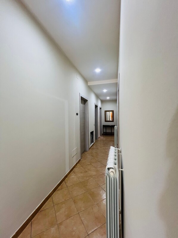 A long, narrow hallway with white walls and a tiled floor. There are several doors along the hallway, and a radiator is visible on the right side. - Villa 3 letti 2 docce e Giardino  (Pizzo)