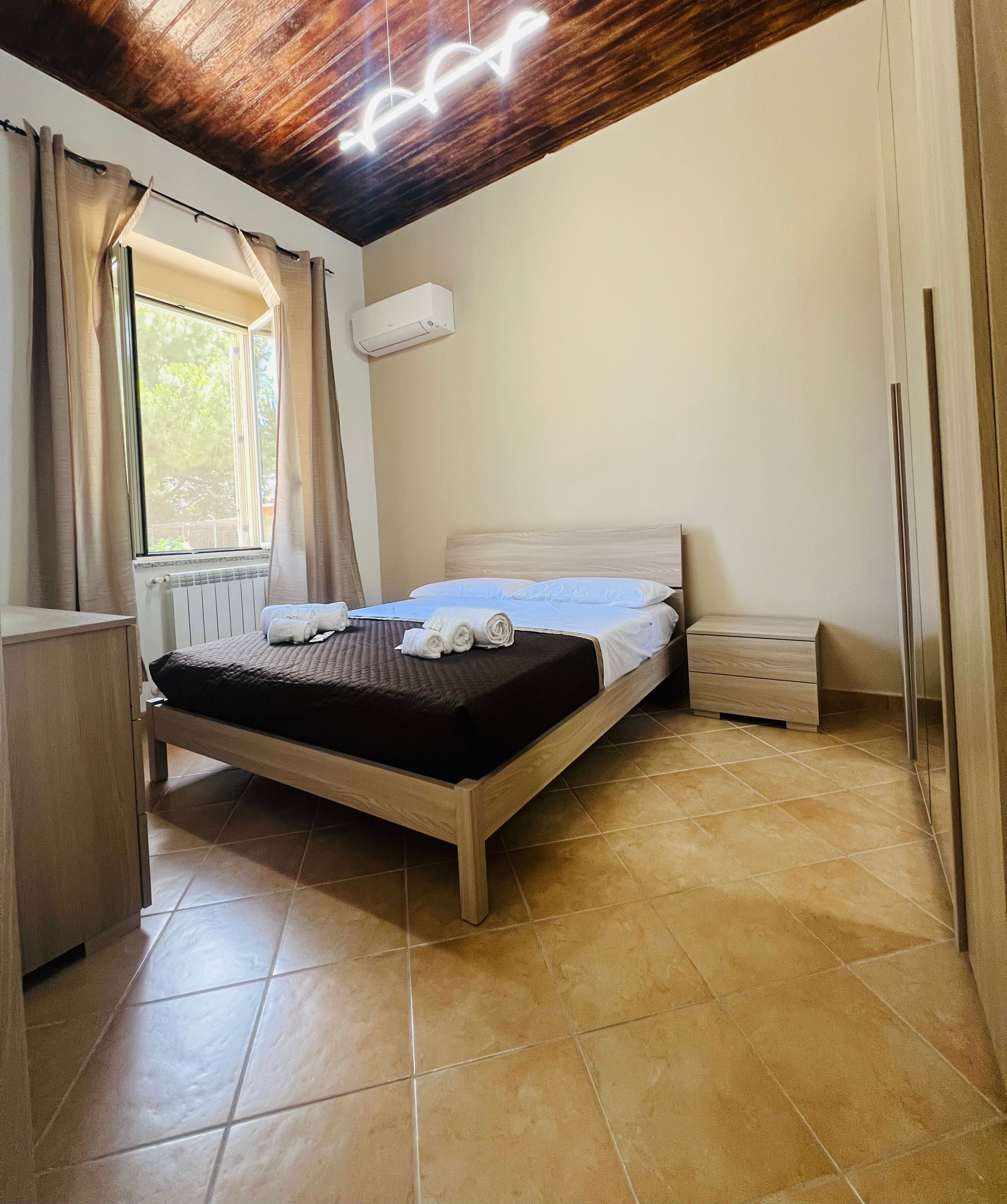 Un dormitorio con cama, mesita de noche, radiador y ventana con cortinas.