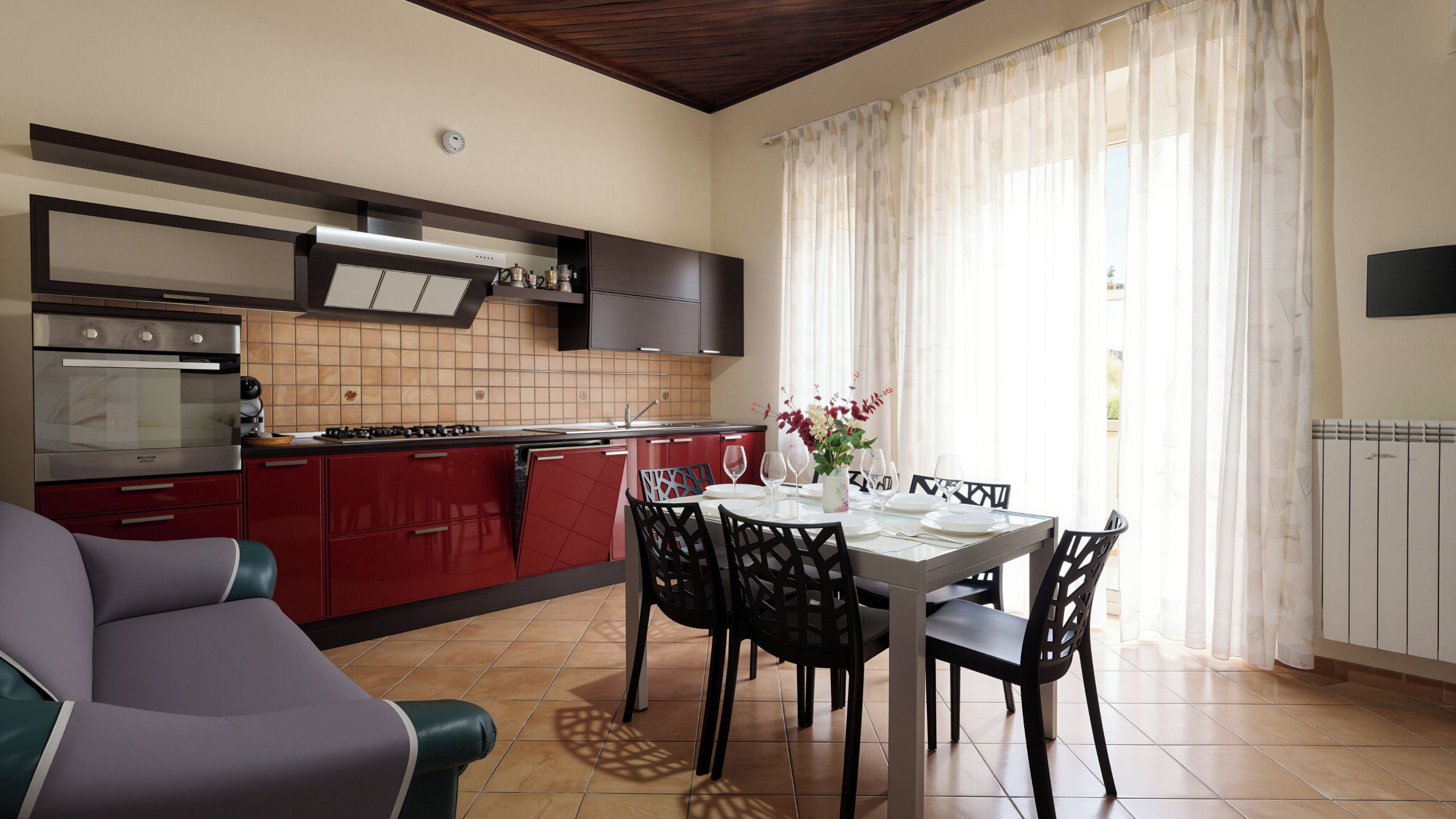 A modern kitchen with red cabinets, a built-in oven, and a dining area with a table set for four.