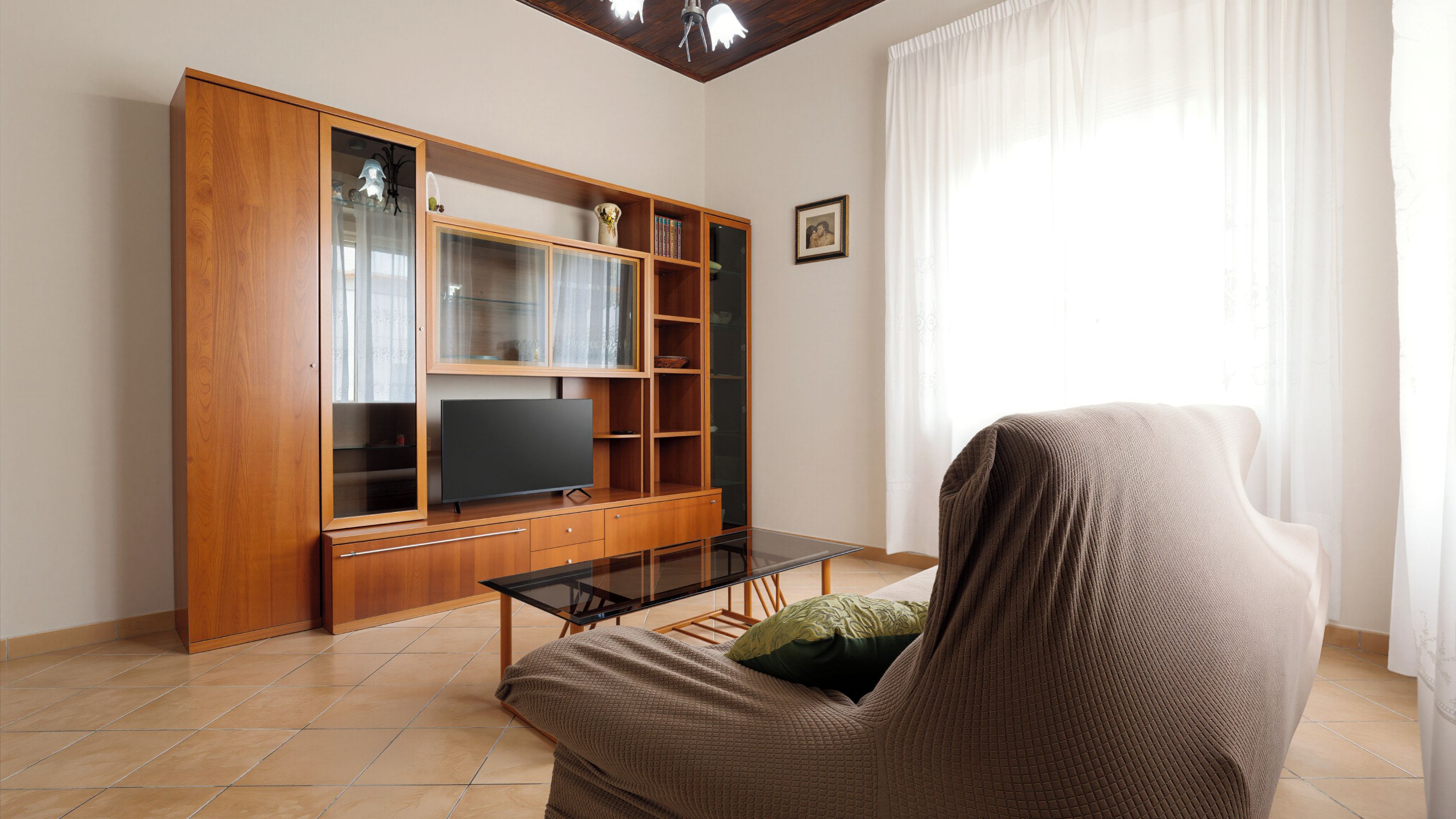 Una sala de estar con un mueble de madera para centro de entretenimiento, un televisor de pantalla plana y un sofá con una manta.