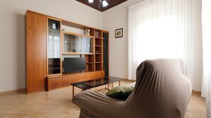 Una sala de estar con un mueble de madera para centro de entretenimiento, un televisor de pantalla plana y un sofá con una manta.