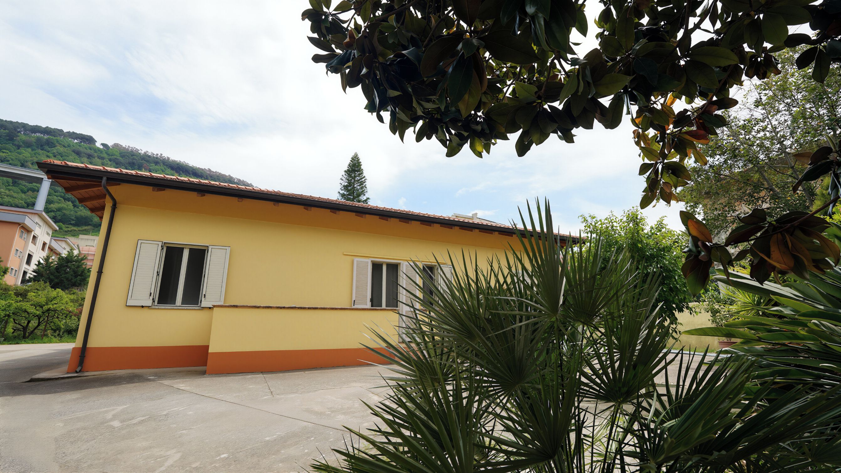 A yellow building with two windows and a red roof.