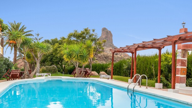 A swimming pool with a wooden pergola, lounge chairs, and a mountain backdrop. - 'Roque Bentayga' with Mountain Views, Wi-Fi, and Air Conditioning (Las Palmas)