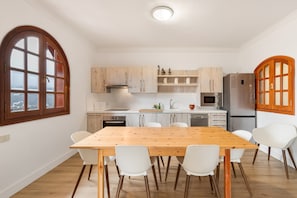 Une cuisine moderne avec une table et des chaises en bois, des appareils électroménagers intégrés et une vue dégagée sur l’extérieur grâce à une grande fenêtre.