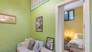 A room with a green wall, a grey sofa with patterned pillows, a small round table with a framed picture, and a bed with a green pillow. - Vacation Apartment 'Guía' with Shared Terrace, Shared Garden and Wi-Fi (Tejeda)