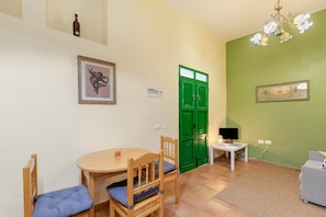 Una habitación con una mesa de comedor, sillas, una puerta verde, un televisor y un sofá.