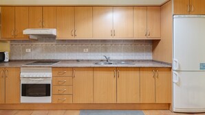 A kitchen with wooden cabinets, a built-in oven, a microwave, a sink, and a refrigerator. - Vacation Apartment 'Guía' with Shared Terrace, Shared Garden and Wi-Fi (Tejeda)