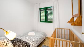 Une chambre à coucher avec un lit, un berceau, une fenêtre avec des volets verts et un miroir fixé au mur.