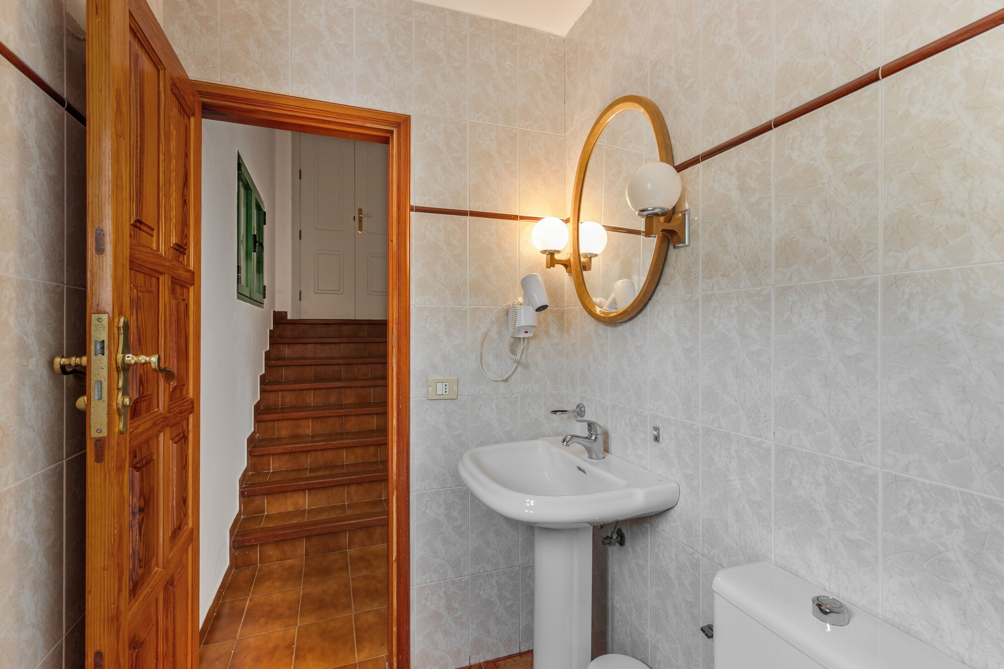Une salle de bain avec une porte en bois, un lavabo blanc, des toilettes et un miroir avec éclairage.