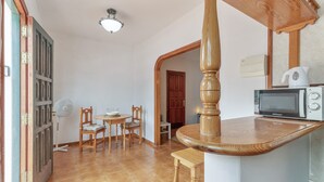 A kitchen with a microwave, wooden chairs, a fan, and a dining table.