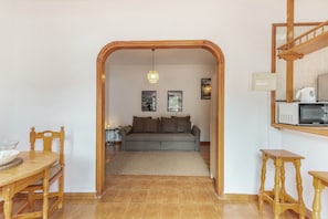Uma sala de estar com sofá, uma mesa de jantar com cadeiras, uma escada de madeira e uma área de cozinha com micro-ondas.