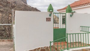 A white building with a green gate, a stone staircase, and a mountain in the background.
