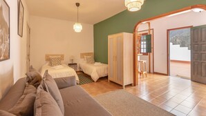 A bedroom with two beds, a sofa, a wardrobe, and a door leading to a balcony.