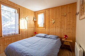 Ein Zimmer mit Holzwänden, einem Bett, zwei Fenstern und Wanddekorationen.