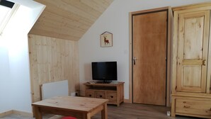 Une pièce avec un plafond en pente, des murs en bois, un téléviseur posé sur un meuble en bois, une porte et un petit placard.
