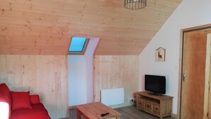 Une pièce chaleureuse avec un plafond en bois, un canapé rouge, une table en bois, un téléviseur posé sur un meuble en bois et une porte avec un cadre en bois.