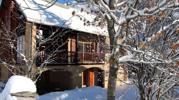Un bâtiment à deux étages doté d’un balcon, des arbres couverts de neige et un ciel dégagé.