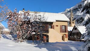 Un bâtiment enneigé avec un balcon, une clôture en bois et une montagne en arrière-plan.