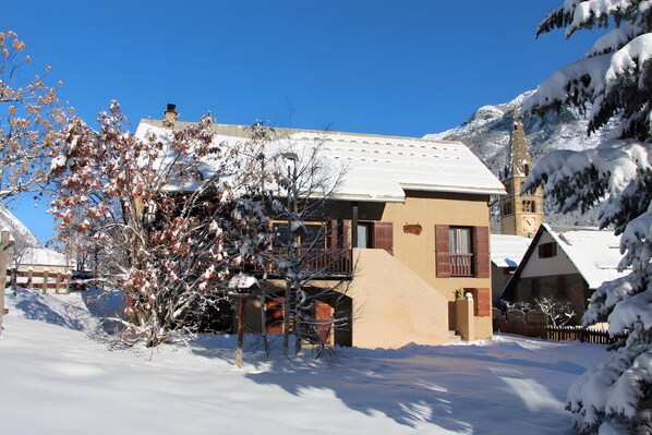 A snow-covered building with a balcony, a wooden fence, and a mountain in the background.
