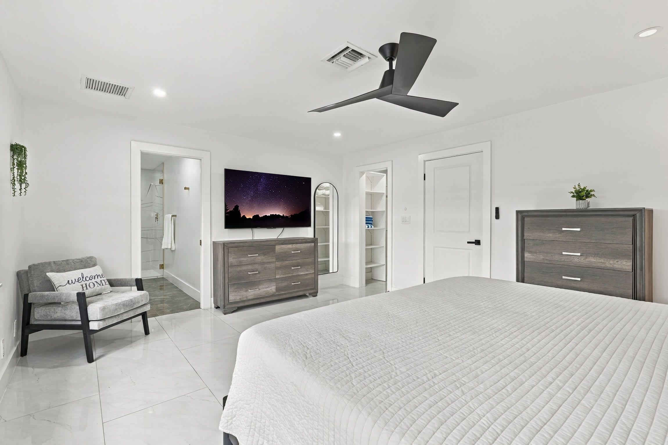 A bedroom with a bed, a chair, a TV, a wardrobe, and a ceiling fan.