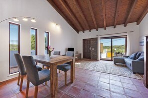 Ein Essbereich mit Holztisch und Stühlen, einer Couch und Blick durch große Fenster.