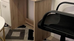 Ein Büro im Eck mit einem Holztisch, einem schwarzen Bürostuhl und einem weißen Schreibtisch mit Schubladen.