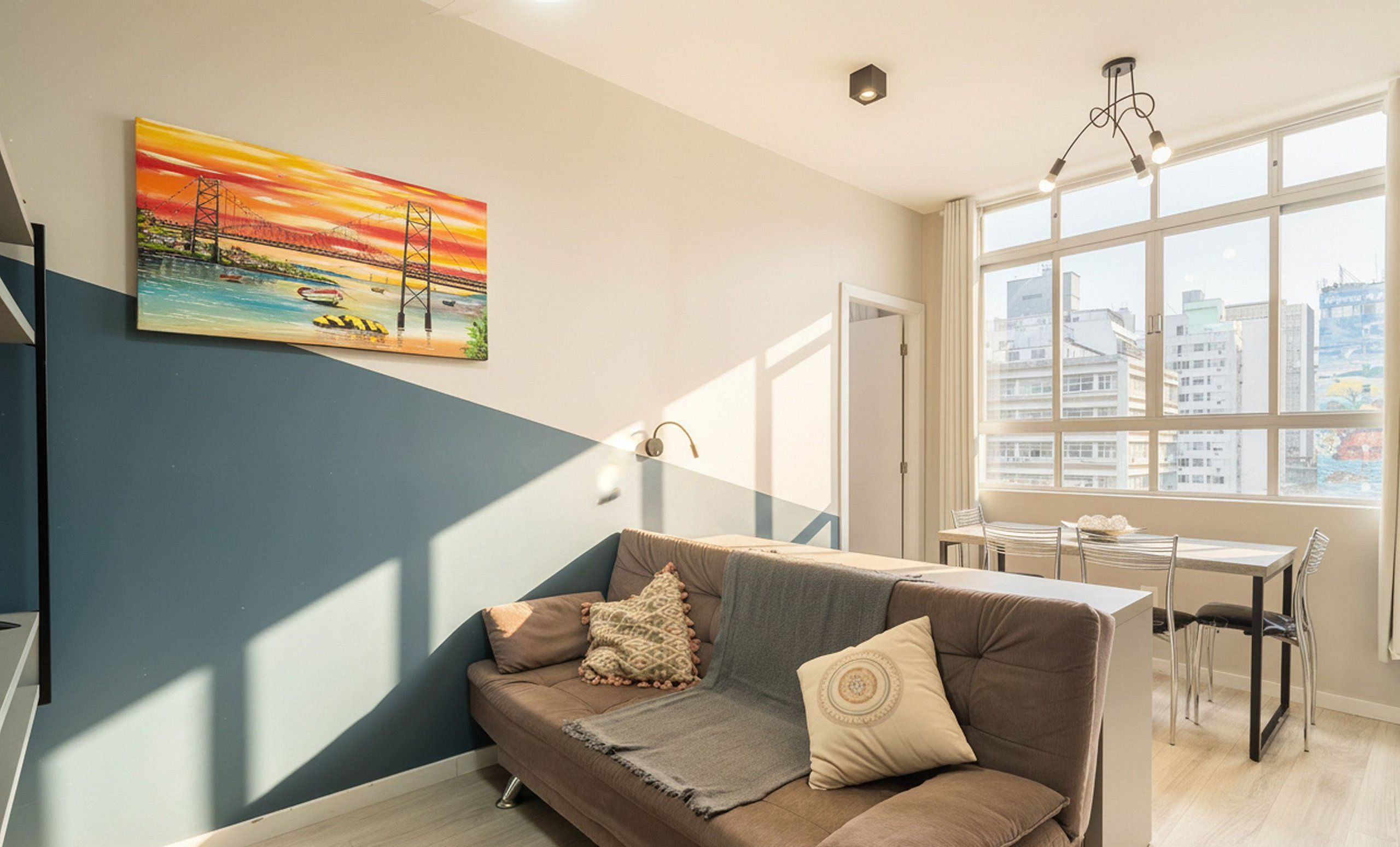 A modern living room with a sofa, a painting of a bridge, and a dining area with a table and chairs.