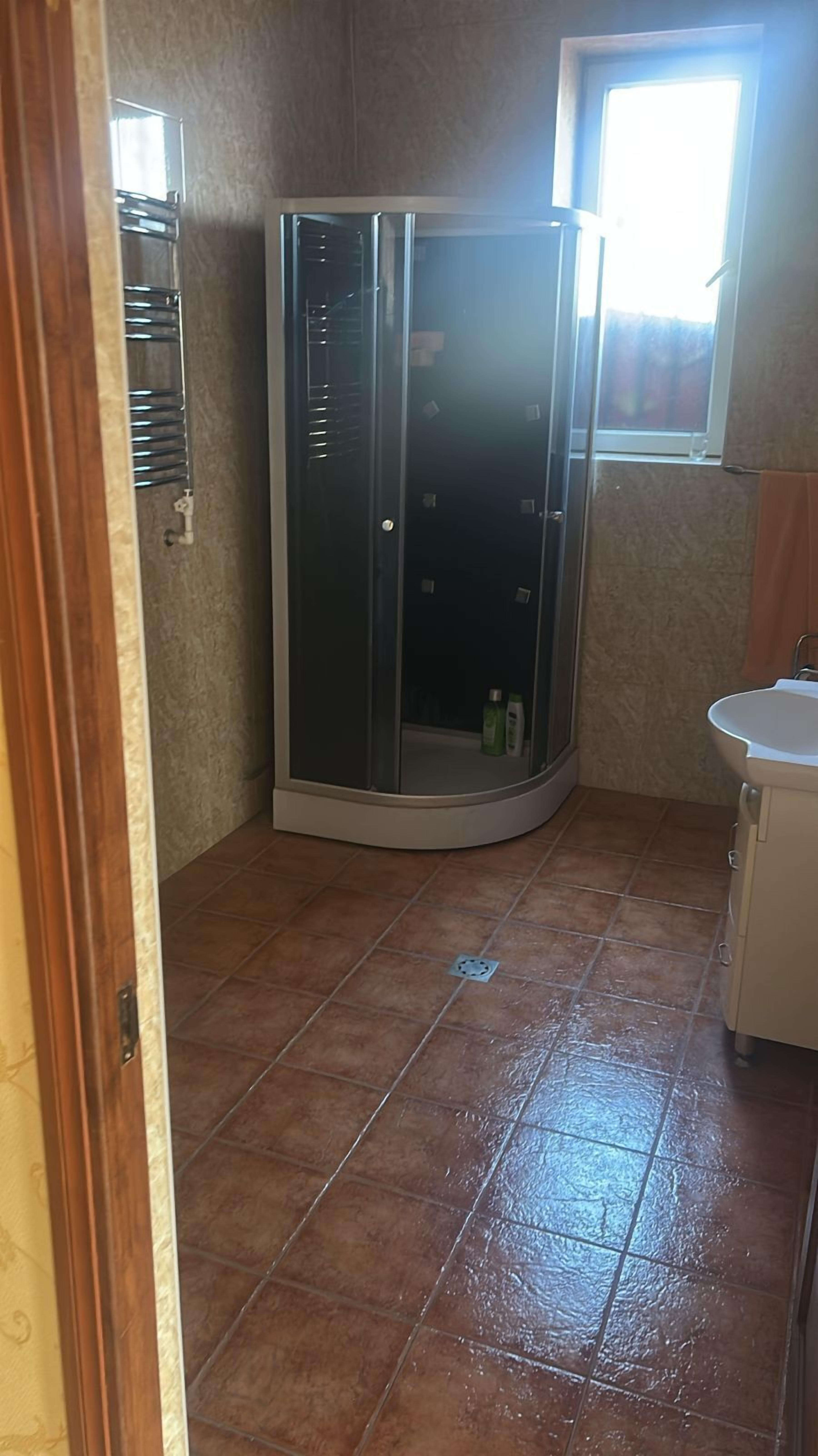 A bathroom with a shower enclosure, a sink, and a window.