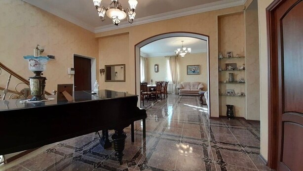 A grand piano in a spacious lobby with a chandelier, marble flooring, and a view into a dining area. - Avan Luxury Villa (Arinj)
