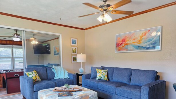 A living room with two blue sofas, a patterned ottoman, a ceiling fan, and a large abstract painting. - Cozy 3br 2ba Winter Haven Getaway Chain of Lakes Downtown (Winter Haven)