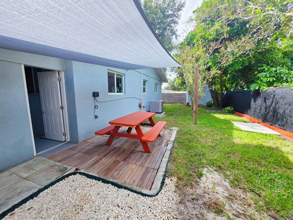 Une maison avec une terrasse en bois, une table de pique-nique rouge et un espace recouvert de gravier.