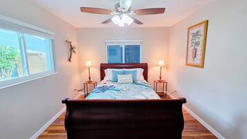 A bedroom with a bed, two bedside lamps, a ceiling fan, a window, and a framed picture on the wall.