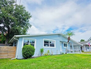 A single-story house with a light blue exterior, a front porch, and a small front yard with a wooden fence and a palm tree.