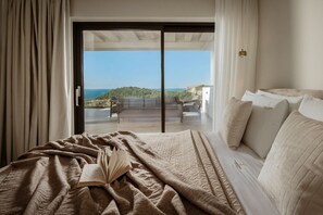 Un dormitorio con una cama grande, vistas al mar y un balcón con mobiliario exterior.