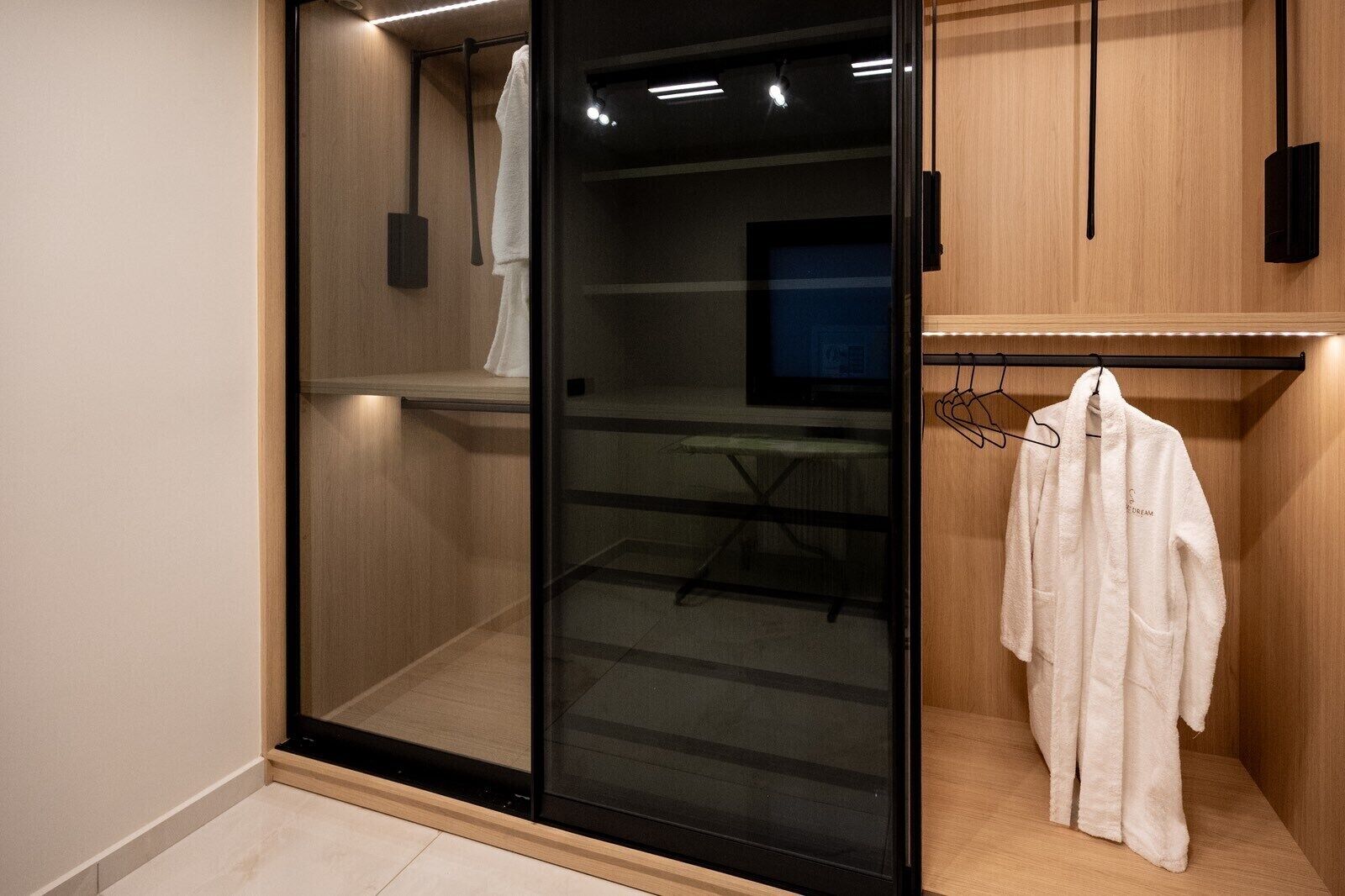 Una habitación moderna con un divisor de vidrio corredero, una bata blanca colgada en un perchero y una mesita con una silla.
