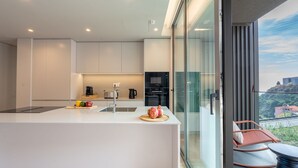 A modern kitchen with a central island, a dining area with a glass wall, and a view of a hill. - Orion Calheta Hills by LovelyStay (Calheta)