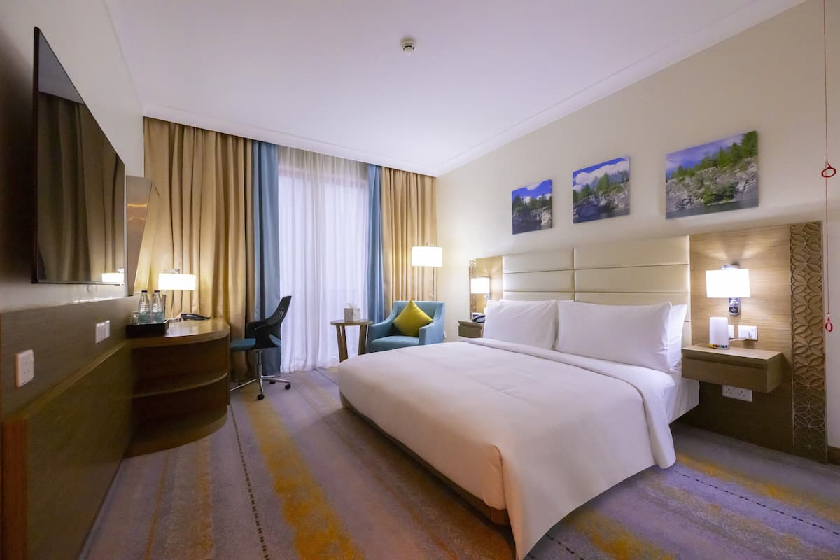 Habitación de hotel con cama, escritorio, silla y un ventanal con cortinas.