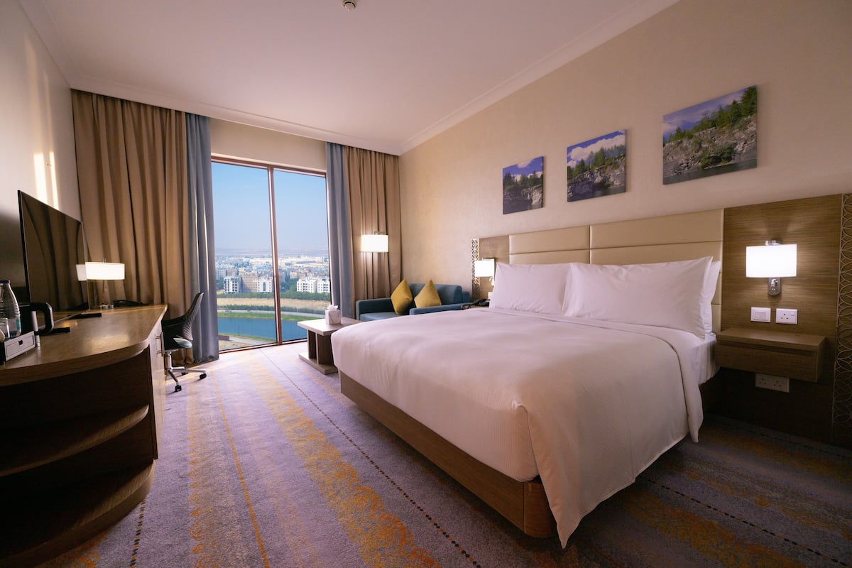 Habitación de hotel con una cama grande, un escritorio con computadora, una silla y vistas a la ciudad.