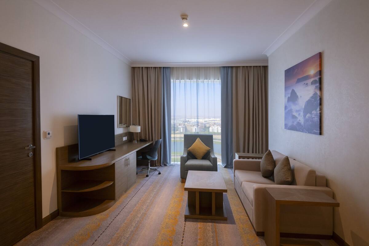 Habitación de hotel con televisión, sofá, escritorio, silla y un cuadro en la pared.