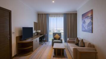 A hotel room with a TV, a sofa, a desk, a chair, and a painting on the wall.