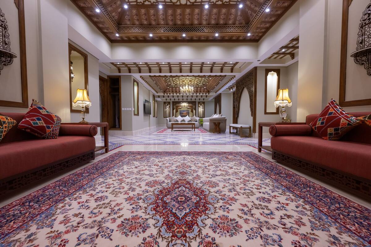 Un vestíbulo espacioso con una alfombra grande y ornamentada, sofás rojos y un candelabro.