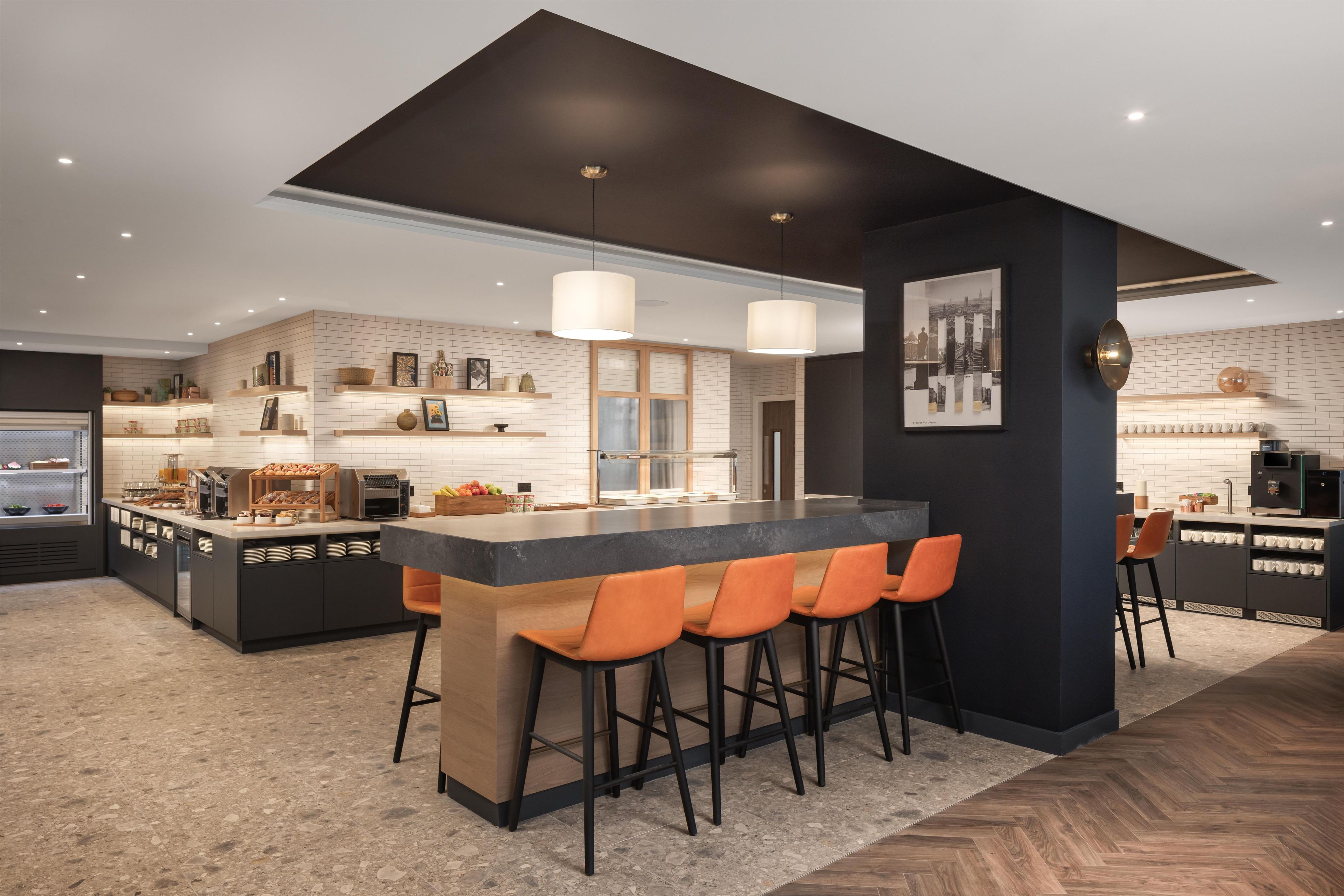 A modern kitchen with a central island, bar stools, pendant lighting, and a herringbone floor pattern.