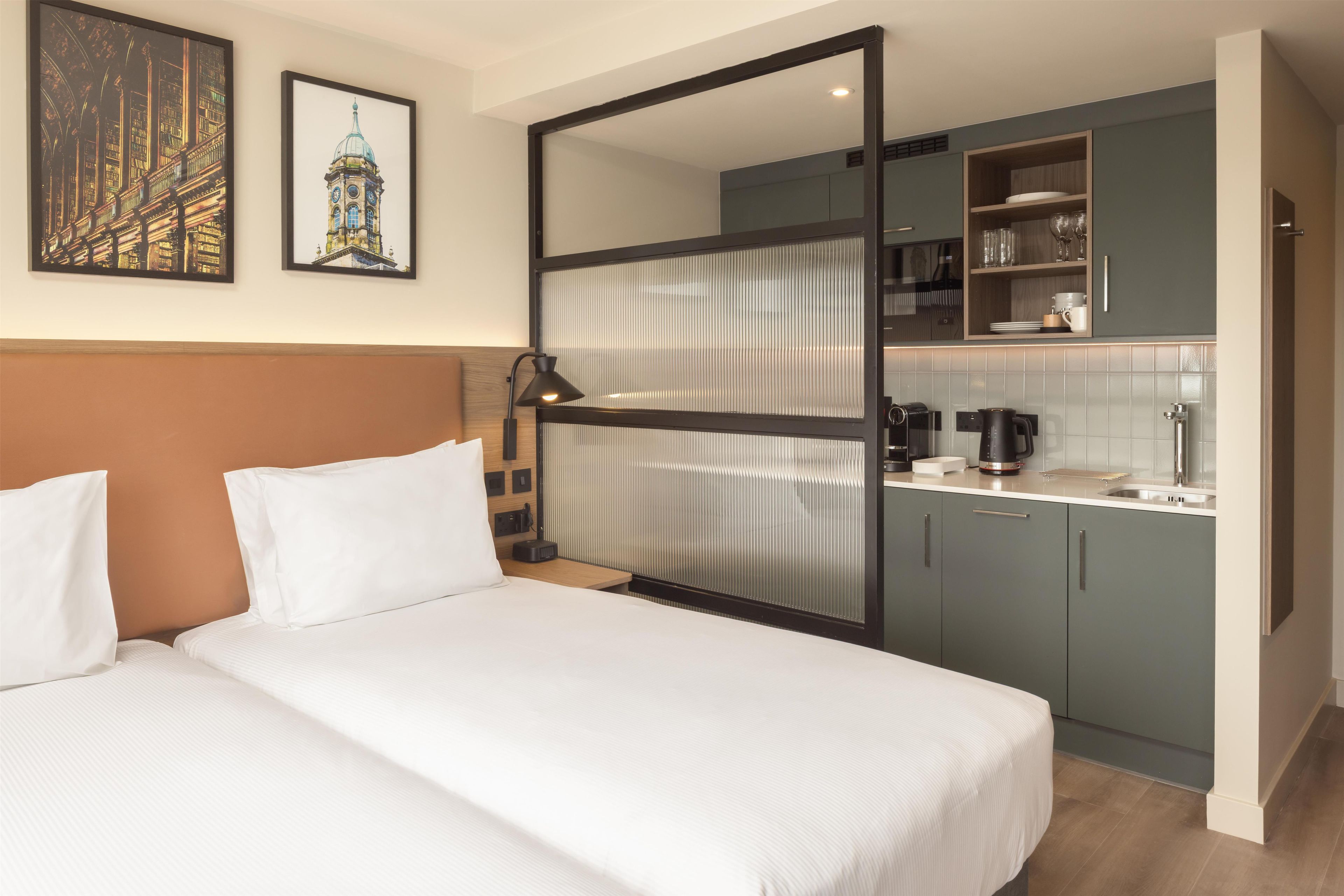 Ein Hotelzimmer mit einem Bett, einem Schreibtisch, einer Küchenzeile und zwei gerahmten Bildern an der Wand.