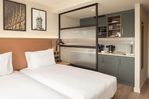 A hotel room with a bed, a desk, a kitchenette, and two framed pictures on the wall. - Home2 Suites By Hilton Dublin City Centre (Dublin)