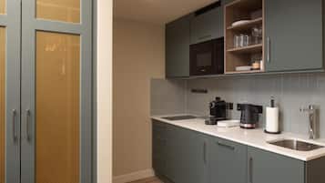 Una cocina con gabinetes grises, microondas, cafetera y pileta.
