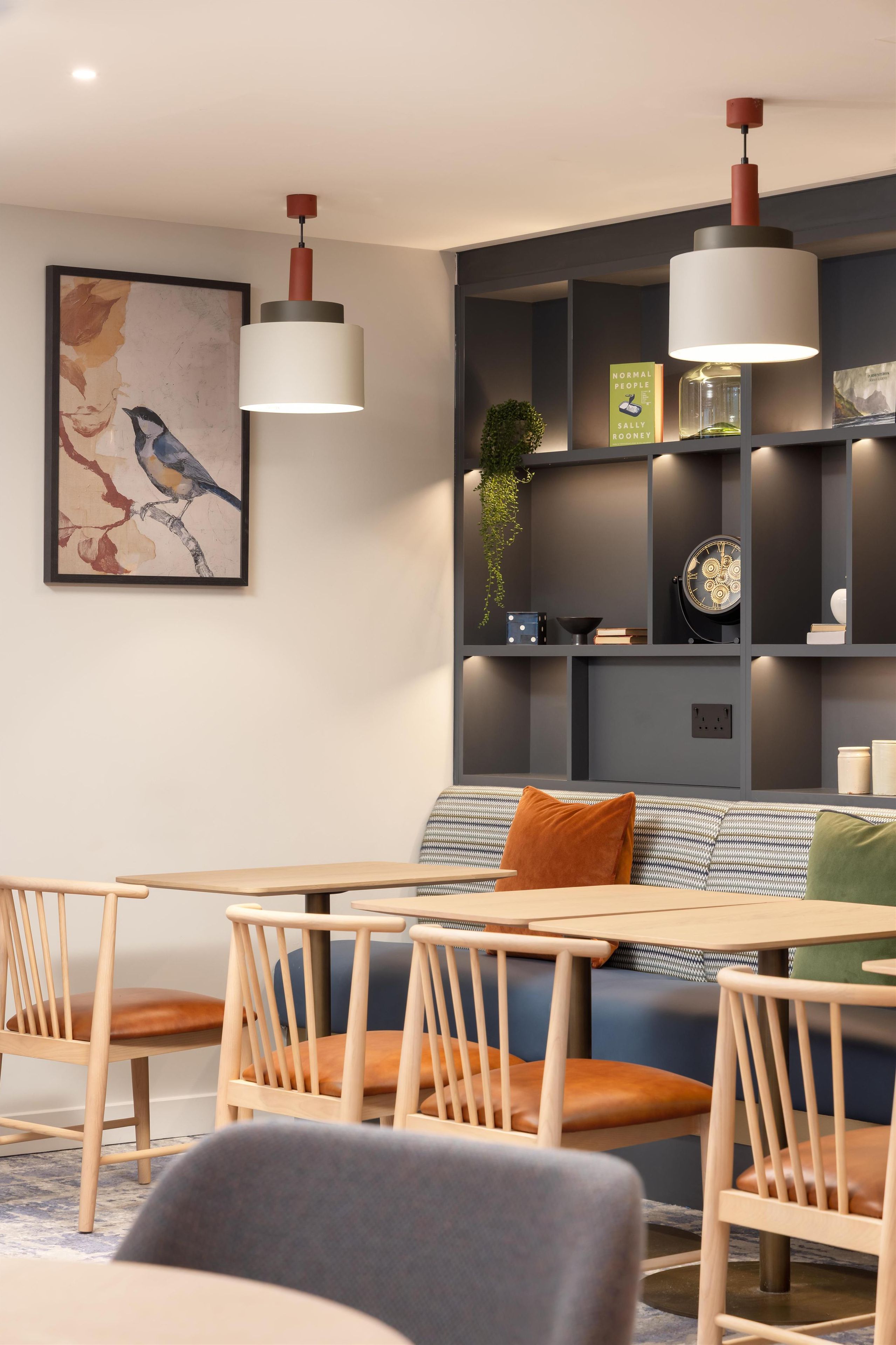 Un espace repas moderne avec une table et des chaises en bois, un canapé bleu et une étagère murale agrémentée d’objets décoratifs.