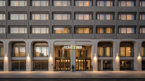 Facciata di un hotel a più piani con un ingresso centrale, ampie finestre e un design architettonico uniforme.