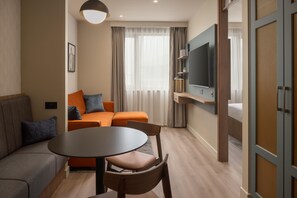 A modern hotel room with a sofa, a dining table, a TV, and a large window with curtains. - Home2 Suites By Hilton Dublin City Centre (Dublin)