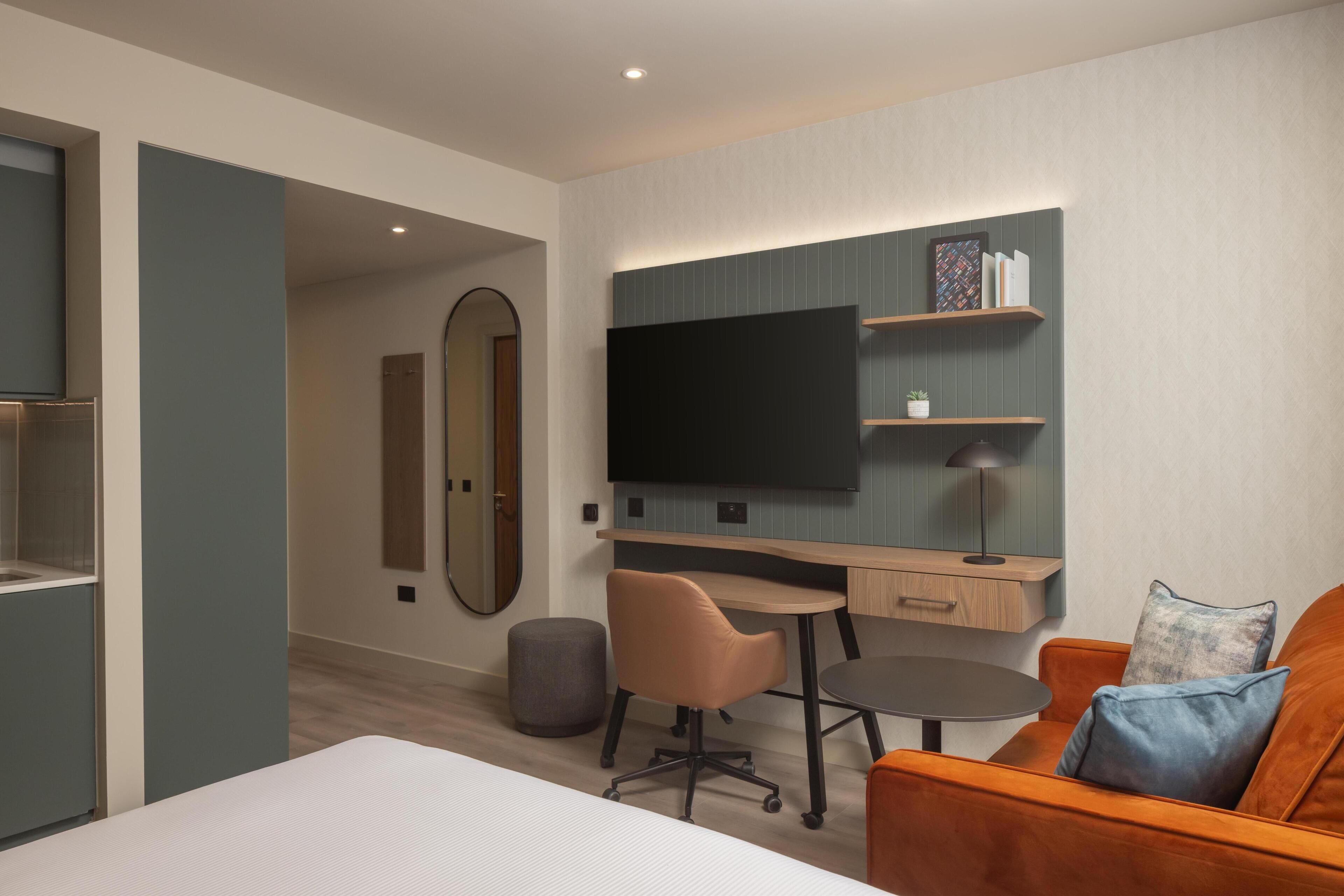 Una habitación de hotel moderna con una cama, un escritorio, una silla, un televisor y un sofá.
