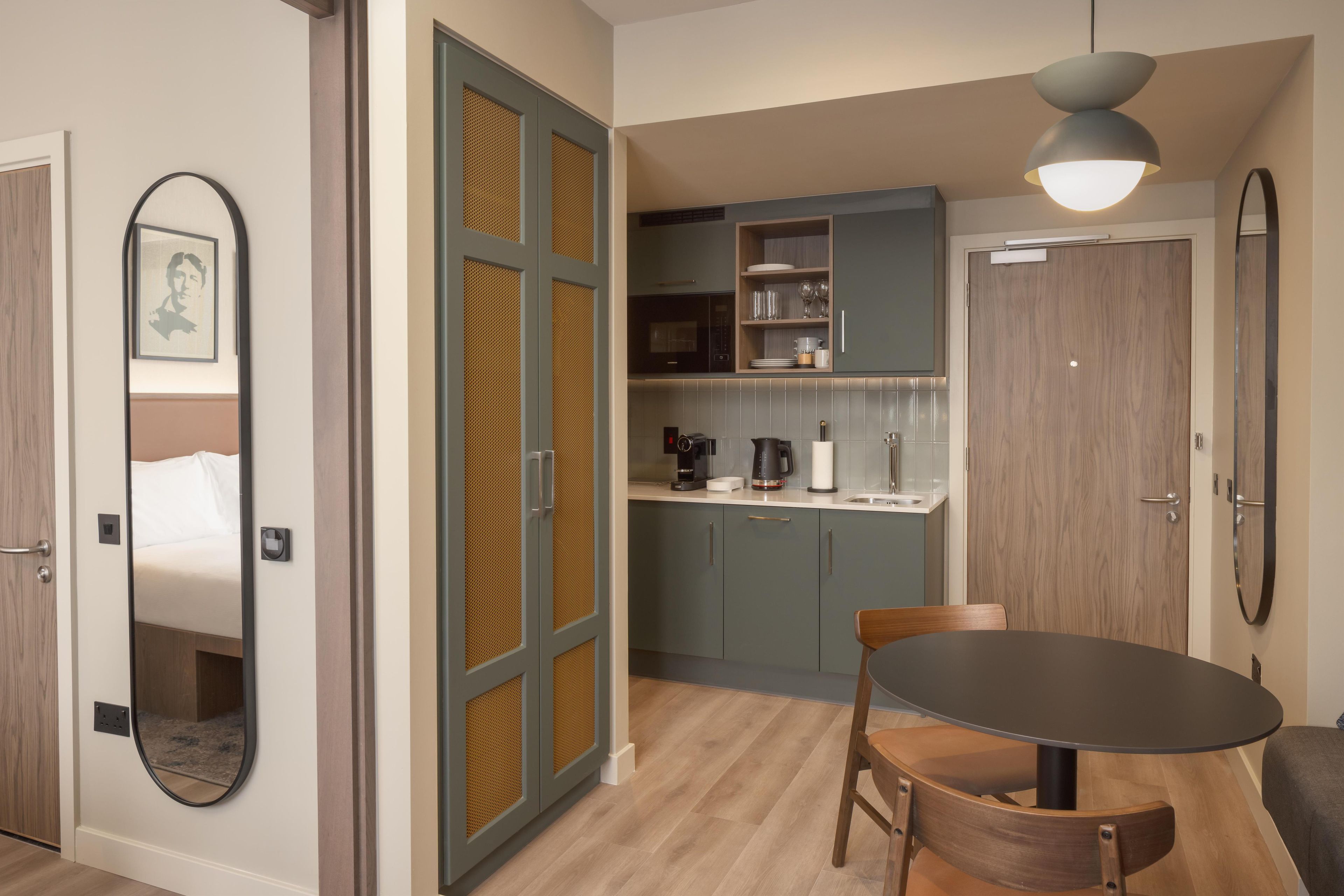 A compact kitchen with a microwave, coffee maker, and cabinets. There is a dining table with chairs and a pendant light above it.